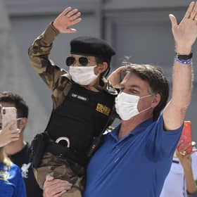 Brazil's President Jair Bolsonaro, wearing a mask, carries a child dressed in a military police uniform during a protest against the National Congress's restrictions and in support of his open-the-economy drive (Picture: Andre Borges/AP)