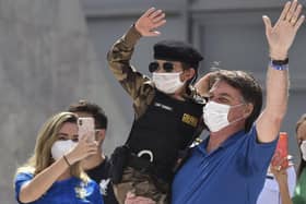 Brazil's President Jair Bolsonaro, wearing a mask, carries a child dressed in a military police uniform during a protest against the National Congress's restrictions and in support of his open-the-economy drive (Picture: Andre Borges/AP)