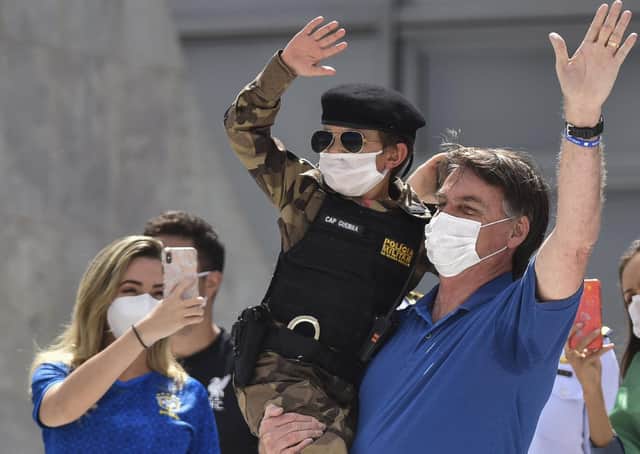 Brazil's President Jair Bolsonaro, wearing a mask, carries a child dressed in a military police uniform during a protest against the National Congress's restrictions and in support of his open-the-economy drive (Picture: Andre Borges/AP)