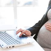 A pregnant businesswoman types out an email on a laptop