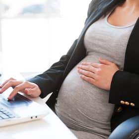 A pregnant businesswoman types out an email on a laptop