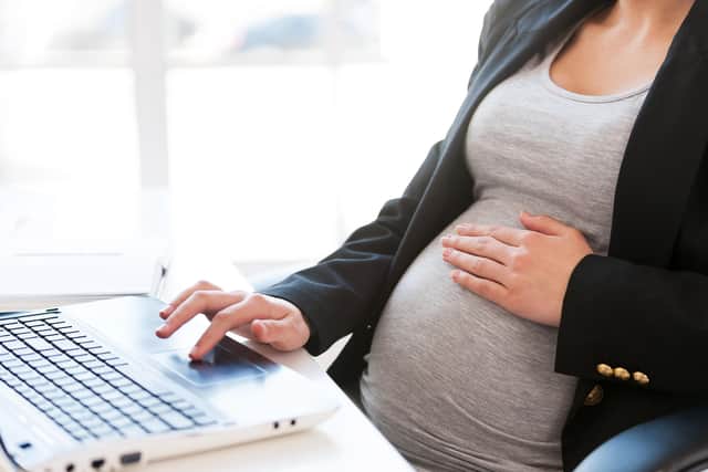 A pregnant businesswoman types out an email on a laptop