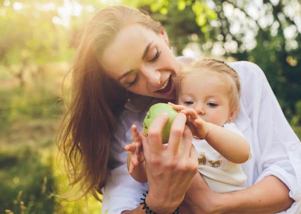 A young girl reaches out for a green apple from her mother