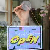 Michelle MacArthur from Moss Flowers in Glasgow displays a "WE'RE OPEN" sign designed by artist Yukai Du