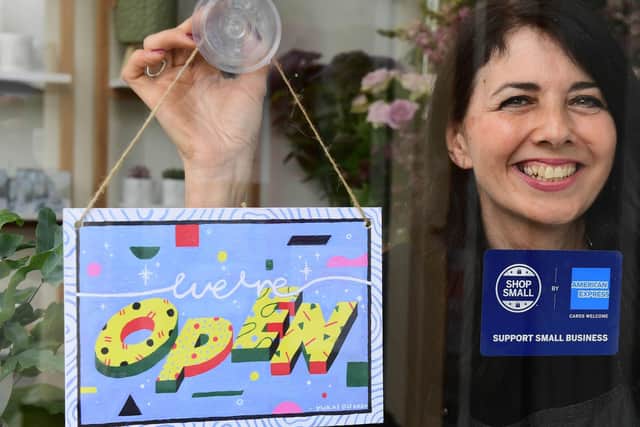 Michelle MacArthur from Moss Flowers in Glasgow displays a "WE'RE OPEN" sign designed by artist Yukai Du