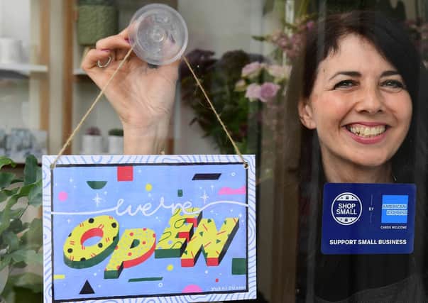 Michelle MacArthur from Moss Flowers in Glasgow displays a "WE'RE OPEN" sign designed by artist Yukai Du