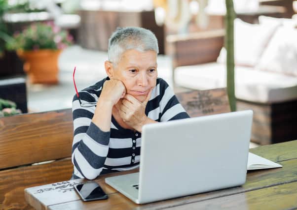 Elderly woman sitting in a cafe, looking at the screen of her laptop, worried