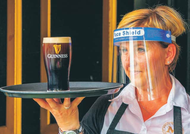 An employee wearing PPE (personal protective equipment) as she serves a customer's pint of Guinness. Picture: Paul Faith/AFP via Getty Images
