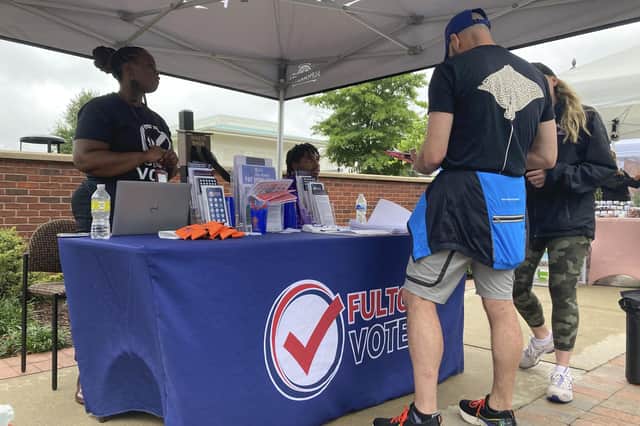 People visit a booth set up by Fulton County to recruit new poll workers at the Alpharetta Farmers Market on Sept. 10, 2022, in Alpharetta, Ga. Lies about the integrity of the 2020 presidential contest by former President Donald Trump and his allies are spurring new interest in working the polls in Georgia and elsewhere in the nation for the upcoming midterm elections. (AP Photo/Sudhin Thanawala)