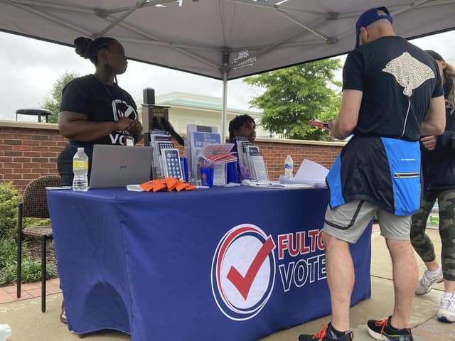People visit a booth set up by Fulton County to recruit new poll workers at the Alpharetta Farmers Market on Sept. 10, 2022, in Alpharetta, Ga. Lies about the integrity of the 2020 presidential contest by former President Donald Trump and his allies are spurring new interest in working the polls in Georgia and elsewhere in the nation for the upcoming midterm elections. (AP Photo/Sudhin Thanawala)
