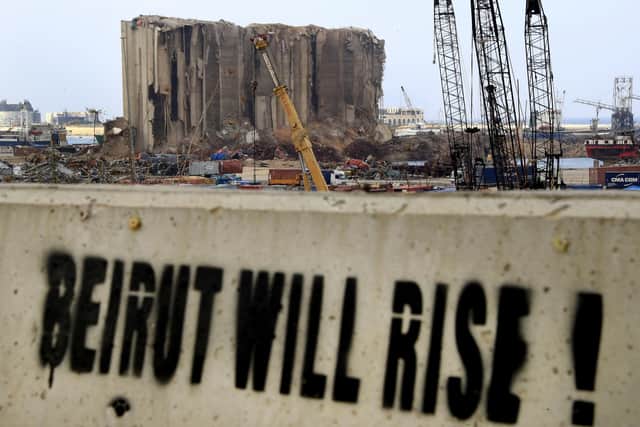 A slogan is painted on a barrier in front of towering grain silos gutted in the massive August explosion at the Beirut port (AP Photo/Hussein Malla).