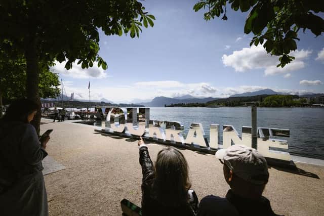 A woman sits on a bench indicates a sign representing Ukraine on the bank of Lake Lucerne in Lucerne as world leaders from countries meet to try to work out a way towards a peace process for Ukraine.