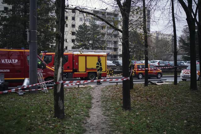 Firefighter stands near ambulance trucks next to apartment buildings seen in background at Le Mas du Taureau neighborhood, in Vauls en Velin, outside Lyon, central France, Friday, Dec. 16, 2022. French authorities say 10 people including five children died in a fire in an apartment building outside the city of Lyon. The cause of the fire is being investigated. (AP Photo/Laurent Cipriani)