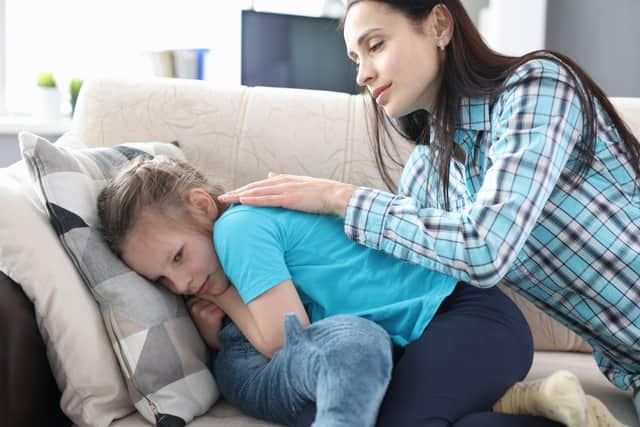 A mother stroking the back and comforting a little girl at home