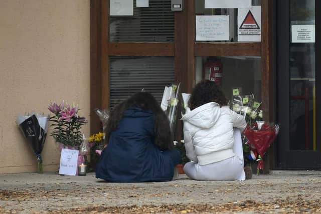 Youngsters sit in front of flowers displayed at the entrance of a middle school in Conflans Saint-Honorine, 30kms northwest of Paris. (Photo by BERTRAND GUAY/AFP via Getty Images)