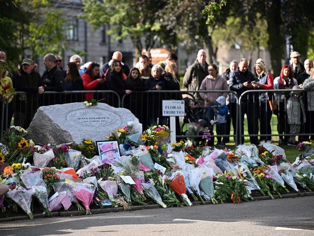 Members of the Public gather by a makeshift memorial to pay respects as they wait for the hearse carrying the coffin of Queen Elizabeth II to pass through Ballater (Photo by PAUL ELLIS/AFP via Getty Images)