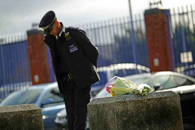 A police officer beside flowers left outside Croydon Custody Centre in south London where a police officer was shot by a man who was being detained in the early hours of Friday morning.