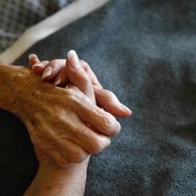 A terminally-ill resident holds a health worker's hand. Picture: Getty Images