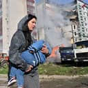 A woman carries her child past residential buildings in Uman, Ukraine, after they were damaged by Russian missile strikes (Picture: Sergei Supinsky/AFP via Getty Images)