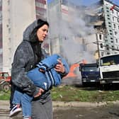 A woman carries her child past residential buildings in Uman, Ukraine, after they were damaged by Russian missile strikes (Picture: Sergei Supinsky/AFP via Getty Images)