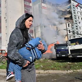 A woman carries her child past residential buildings in Uman, Ukraine, after they were damaged by Russian missile strikes (Picture: Sergei Supinsky/AFP via Getty Images)