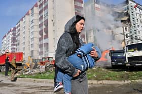 A woman carries her child past residential buildings in Uman, Ukraine, after they were damaged by Russian missile strikes (Picture: Sergei Supinsky/AFP via Getty Images)