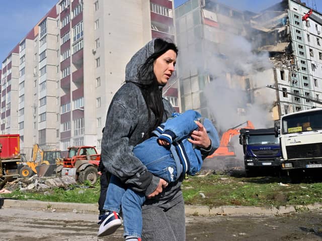 A woman carries her child past residential buildings in Uman, Ukraine, after they were damaged by Russian missile strikes (Picture: Sergei Supinsky/AFP via Getty Images)