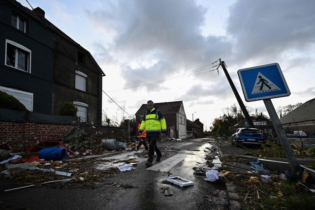 Municipal workers walk past damages in Bihucourt, northern France, on October 24, 2022 after a tornado hit the region. (Photo by Sameer Al-Doumy / AFP)