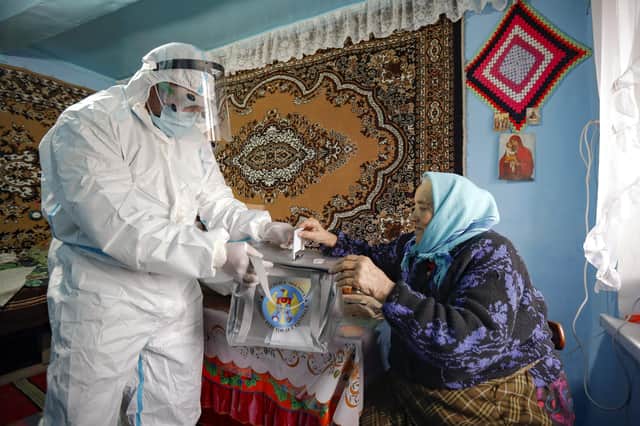 An election official, wearing a biohazard suit for protection against Covid-19, collects a vote in a mobile ballot box from an elderly woman during the presidential elections in Moldova (Picture: Roveliu Buga/AP)
