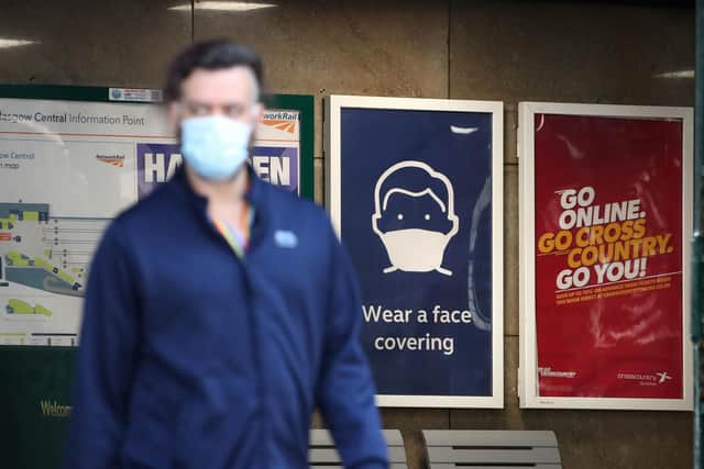 A passenger wearing a face mask walks past a sign at the entrance to Glasgow Central Station as Scotland continues to lift coronavirus lockdown measures.