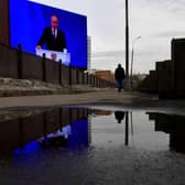 A man walks past a huge screen displaying the broadcast of Russia's President Vladimir Putin's annual state of the nation address on the facade of a building in Moscow.