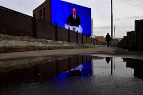 A man walks past a huge screen displaying the broadcast of Russia's President Vladimir Putin's annual state of the nation address on the facade of a building in Moscow.