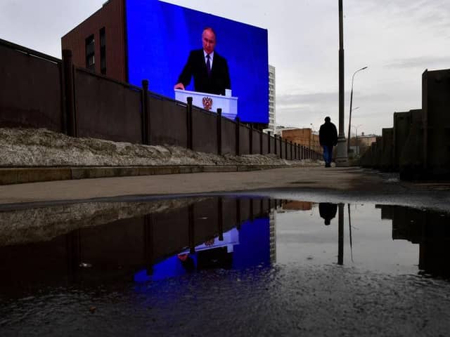 A man walks past a huge screen displaying the broadcast of Russia's President Vladimir Putin's annual state of the nation address on the facade of a building in Moscow.