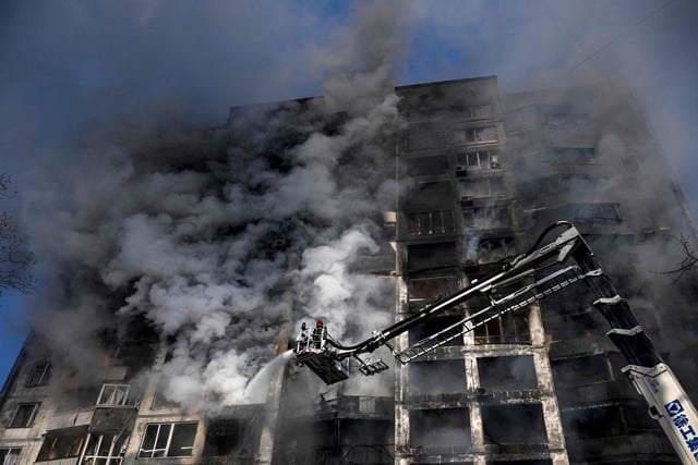Firefighters stand on a crane to extinguish a fire in an apartment building in Kyiv on March 15, 2022, after strikes on residential areas killed at least two people,  A series of powerful explosions rocked residential districts of Kyiv early today just hours before talks between Ukraine and Russia were set to resume. (Photo by Aris Messinis / AFP) (Photo by ARIS MESSINIS/AFP via Getty Images)