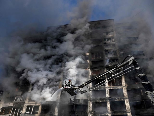 Firefighters stand on a crane to extinguish a fire in an apartment building in Kyiv on March 15, 2022, after strikes on residential areas killed at least two people,  A series of powerful explosions rocked residential districts of Kyiv early today just hours before talks between Ukraine and Russia were set to resume. (Photo by Aris Messinis / AFP) (Photo by ARIS MESSINIS/AFP via Getty Images)
