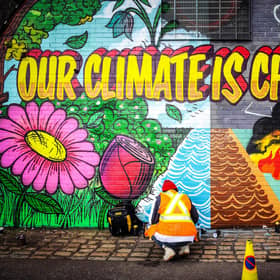 Street artists Ciaran Globel and Conzo Throb paint a mural designed by Colin Li, 14, on a wall opposite the COP26 climate summit venue in Glasgow in 2021 (Picture: Andy Buchanan/AFP via Getty Images)