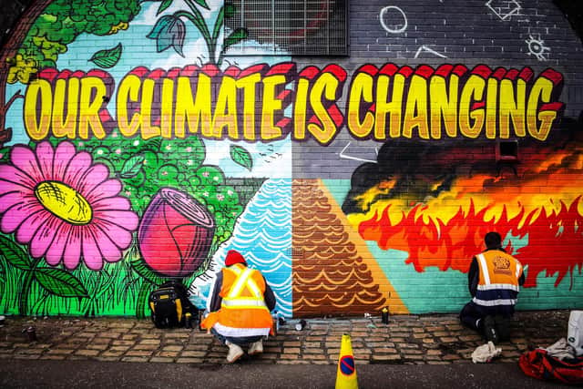 Street artists Ciaran Globel and Conzo Throb paint a mural designed by Colin Li, 14, on a wall opposite the COP26 climate summit venue in Glasgow in 2021 (Picture: Andy Buchanan/AFP via Getty Images)