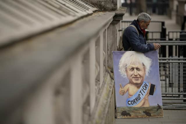 Political artist Kaya Mar holds one of his paintings of British Prime Minister Boris Johnson near the entrance to Downing Street, before Mr Johnson was driven past to go to the Houses of Parliament. Picture: AP Photo/Matt Dunham