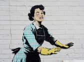 Undated handout file photo of one of the new works by Banksy, appears to show a 1950's housewife, wearing a classic blue pinny and yellow washing up gloves, with a swollen eye and a missing tooth seemingly shoving her male partner into a chest freezer, the piece is set on a white wall backdrop in Kent. Issue date: Tuesday February 14, 2023.