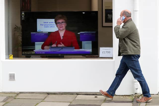 A member of the public walks past a TV screen at The Sound Counsel in Edinburgh as First Minister Nicola Sturgeon takes part in a virtual sitting of the Scottish Parliament. Picture: Andrew Milligan/PA Wire