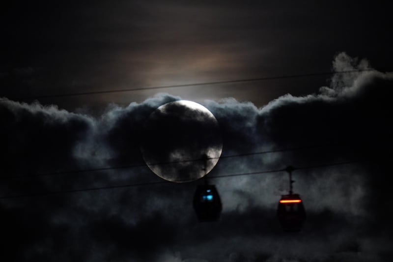 The super blue moon hidden behind clouds as IFS Cloud Cable Cars pass by at Greenwich. Photo: Yui Mok/PA Wire