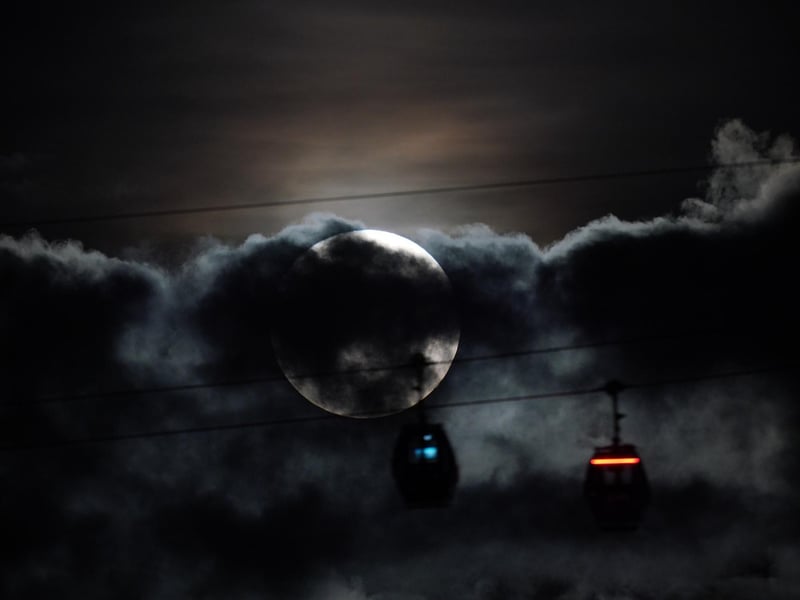 The super blue moon hidden behind clouds as IFS Cloud Cable Cars pass by at Greenwich. Photo: Yui Mok/PA Wire