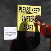 A worker installs a sign asking people to social distance at a walk-through Covid-19 testing centre in Glasgow. Photo by ANDREW MILLIGAN/POOL/AFP via Getty Images