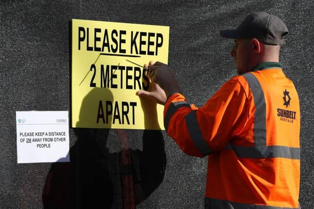 A worker installs a sign asking people to social distance at a walk-through Covid-19 testing centre in Glasgow. Photo by ANDREW MILLIGAN/POOL/AFP via Getty Images