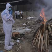 A man wearing personal protective equipment prays in front of the burning funeral pyre of his father who died of COVID-19, at a crematorium in New Delhi, India (AP Photo/Amit Sharma).