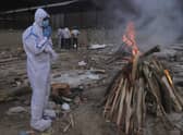 A man wearing personal protective equipment prays in front of the burning funeral pyre of his father who died of COVID-19, at a crematorium in New Delhi, India (AP Photo/Amit Sharma).