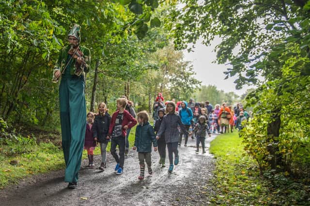 A stilt walker leads a group of children walking in the woods at Craigmillar Castle Park