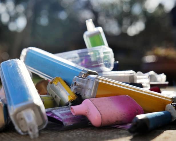 Discarded electronic cigarette vapes that have been collected from roads and pavements shot over a pale concrete slab background