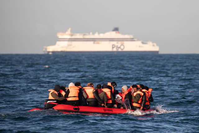 Migrants packed into a small inflatable boat bail water out as they attempt to cross the English Channel off the coast of Dover, England (Picture: Luke Dray/Getty Images)