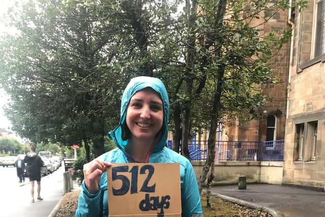 Mhairi Taylor on a rainy day, holding up a sign showing how many days the Couper Institute library had then been closed.